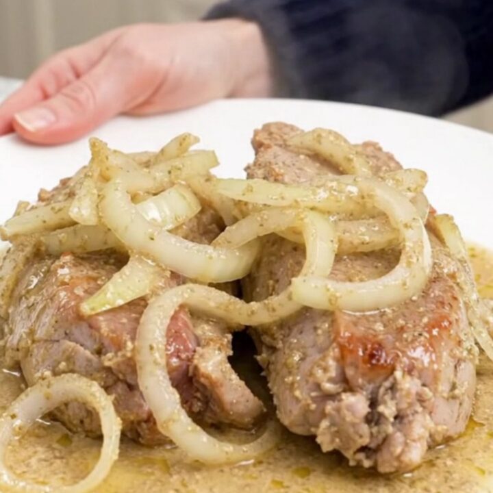 A close-up view of cooked pork tenderloin slices topped with a thick, creamy horseradish sauce on a white plate.