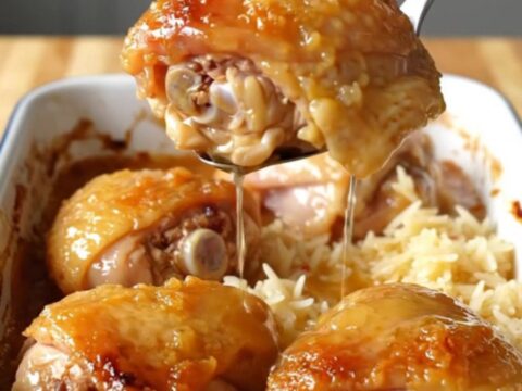 A large white enameled baking dish filled with golden-brown chicken thighs nestled over fluffy white rice in a honey glaze.