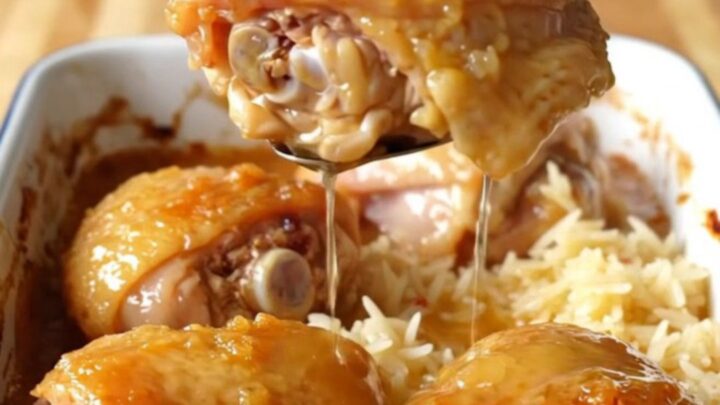 A large white enameled baking dish filled with golden-brown chicken thighs nestled over fluffy white rice in a honey glaze.