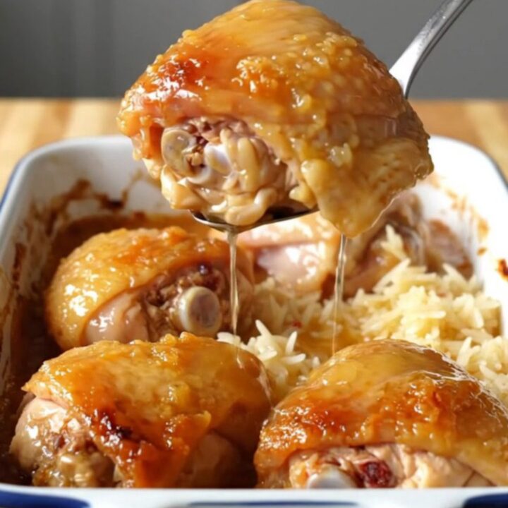 A large white enameled baking dish filled with golden-brown chicken thighs nestled over fluffy white rice in a honey glaze.
