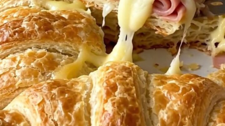 Golden brown baked crescent sliders in a white rectangular dish, showing flaky layers and melted cheese.