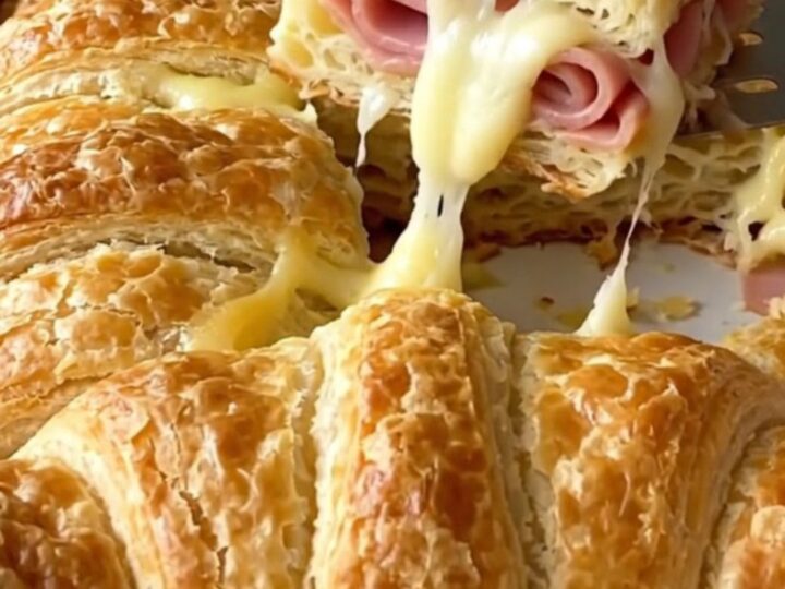 Golden brown baked crescent sliders in a white rectangular dish, showing flaky layers and melted cheese.