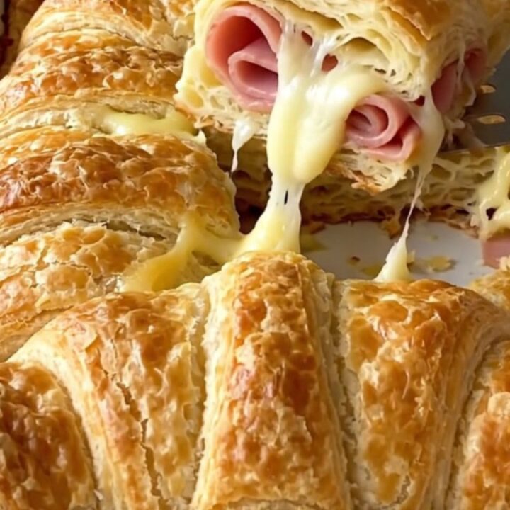 Golden brown baked crescent sliders in a white rectangular dish, showing flaky layers and melted cheese.