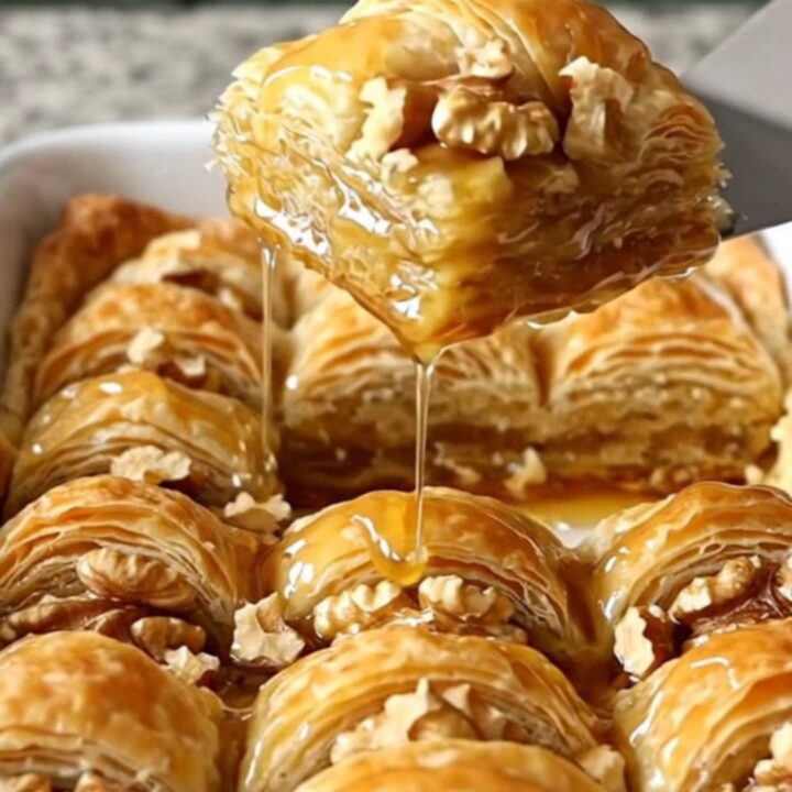 A golden, square-cut honey walnut crescent baklava bar held by a hand, showing crispy layers.