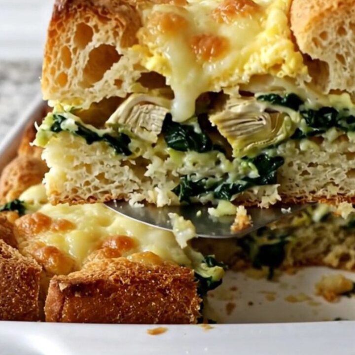 A golden-brown, freshly baked spinach artichoke breakfast strata in a white ceramic dish.