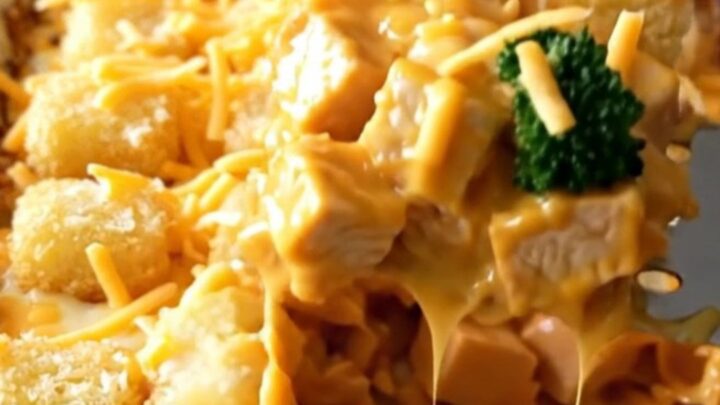 A golden, bubbling broccoli cheddar chicken bake in a white ceramic dish.