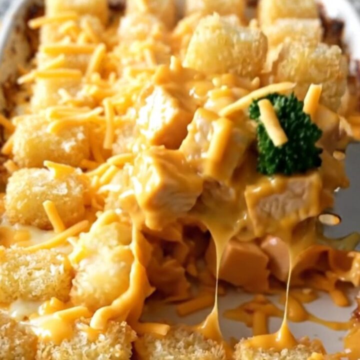 A golden, bubbling broccoli cheddar chicken bake in a white ceramic dish.