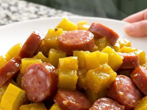 A close-up view of the slow cooker filled with layers of sliced yellow squash, onions, and smoked sausage coins.