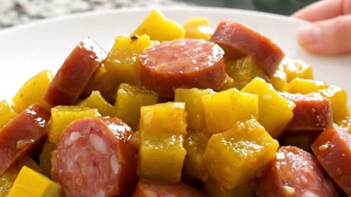 A close-up view of the slow cooker filled with layers of sliced yellow squash, onions, and smoked sausage coins.