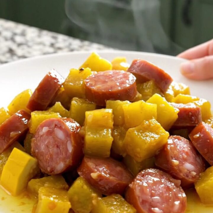 A close-up view of the slow cooker filled with layers of sliced yellow squash, onions, and smoked sausage coins.