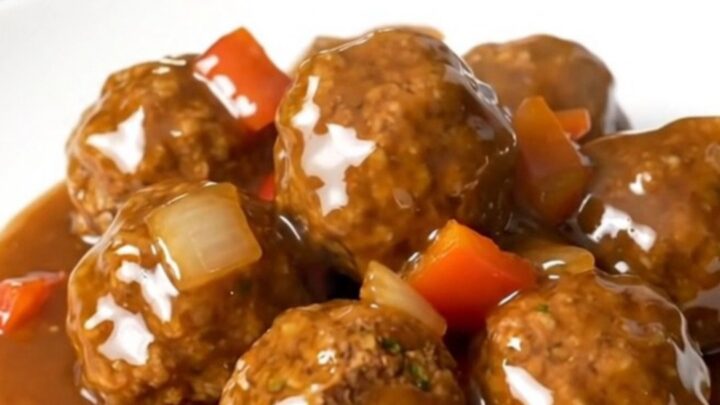 A plate of Crockpot Cajun Honey Turkey Meatballs glazed in a thick, shiny sauce with visible pieces of peppers and onions.