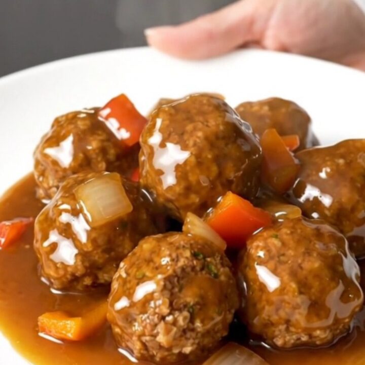 A plate of Crockpot Cajun Honey Turkey Meatballs glazed in a thick, shiny sauce with visible pieces of peppers and onions.