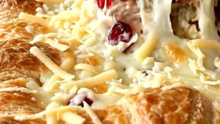 A golden-brown turkey and cranberry crescent bake in a white baking dish on a white quartz counter.