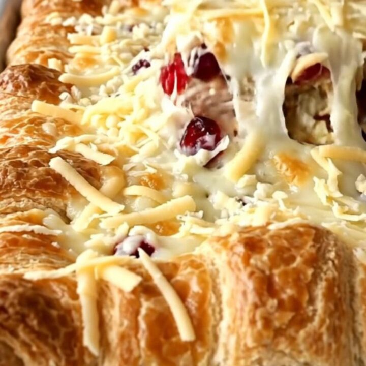 A golden-brown turkey and cranberry crescent bake in a white baking dish on a white quartz counter.