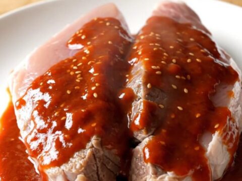 A slow-cooked pork tenderloin with a glossy, deep red gochujang honey glaze on a white plate.