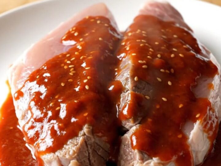 A slow-cooked pork tenderloin with a glossy, deep red gochujang honey glaze on a white plate.