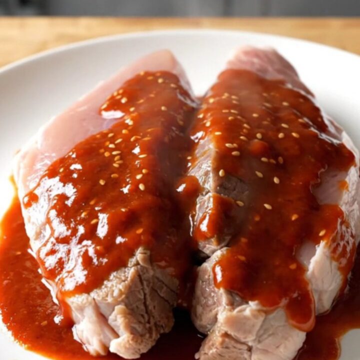 A slow-cooked pork tenderloin with a glossy, deep red gochujang honey glaze on a white plate.