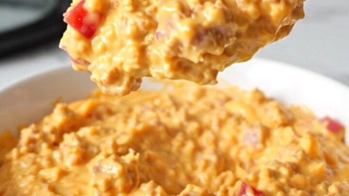 A creamy, orange-hued sausage and pimento cheese dip served in a white bowl with steam rising.