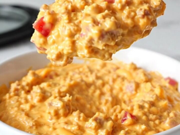 A creamy, orange-hued sausage and pimento cheese dip served in a white bowl with steam rising.