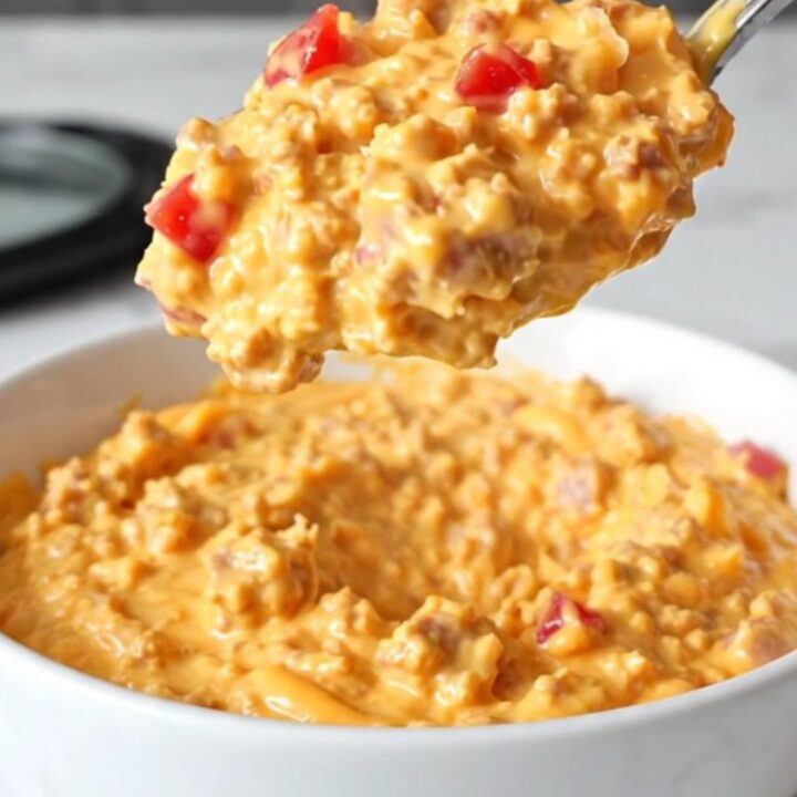 A creamy, orange-hued sausage and pimento cheese dip served in a white bowl with steam rising.
