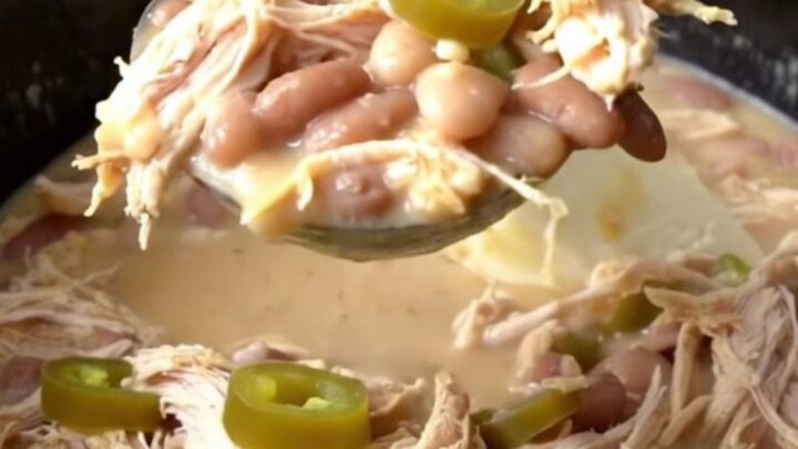 A close-up of creamy white chicken chili in a black slow cooker insert, topped with fresh jalapeño slices.