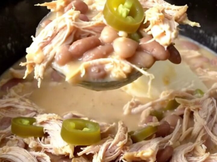 A close-up of creamy white chicken chili in a black slow cooker insert, topped with fresh jalapeño slices.