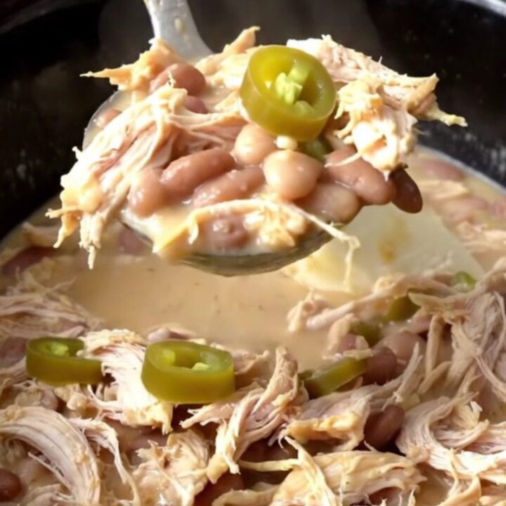 A close-up of creamy white chicken chili in a black slow cooker insert, topped with fresh jalapeño slices.