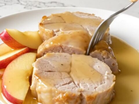 Slices of tender, golden-cooked pork tenderloin served with soft apple wedges and a rich honey apple sauce on a white plate.