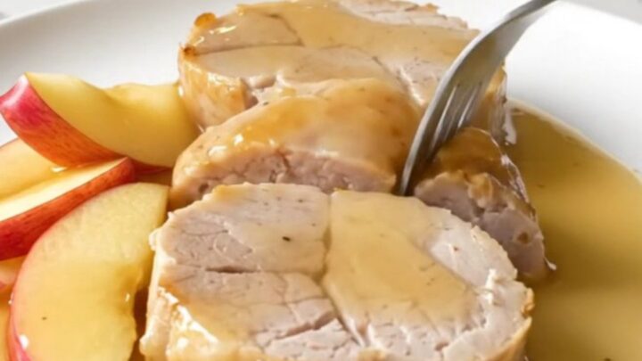 Slices of tender, golden-cooked pork tenderloin served with soft apple wedges and a rich honey apple sauce on a white plate.