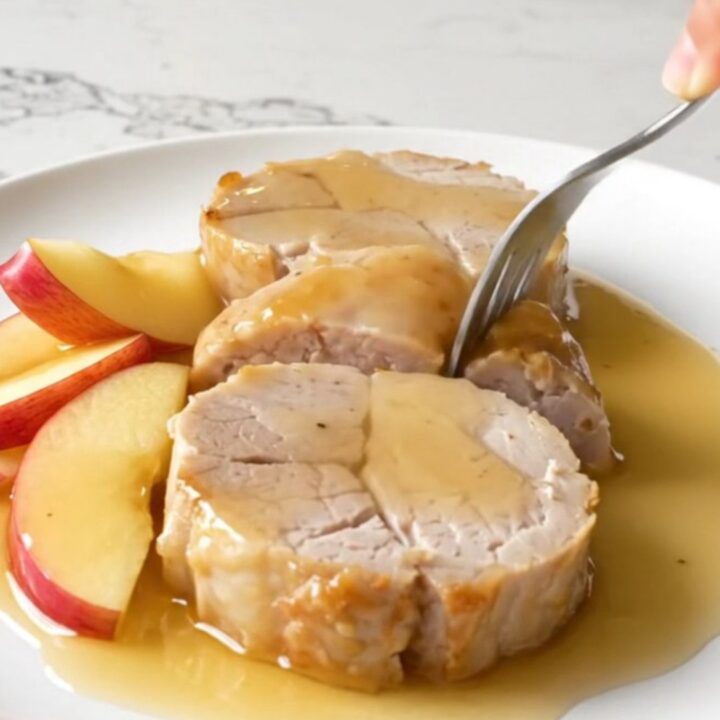 Slices of tender, golden-cooked pork tenderloin served with soft apple wedges and a rich honey apple sauce on a white plate.