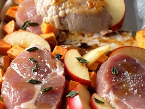 A sheet pan filled with golden-brown pork medallions, roasted sweet potato cubes, and tender red apple wedges.