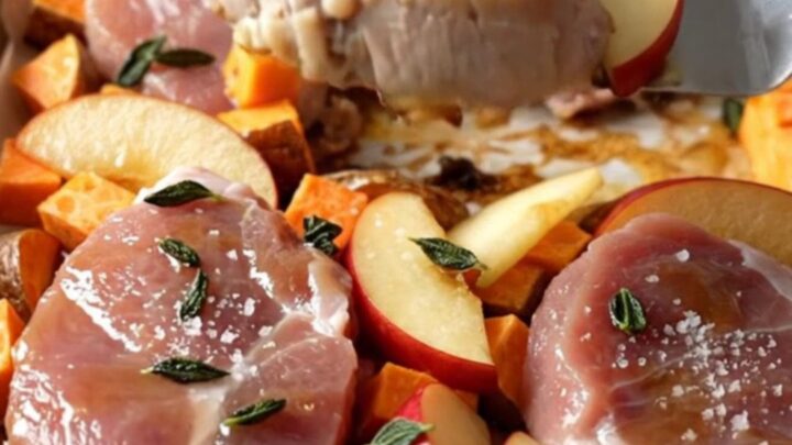 A sheet pan filled with golden-brown pork medallions, roasted sweet potato cubes, and tender red apple wedges.
