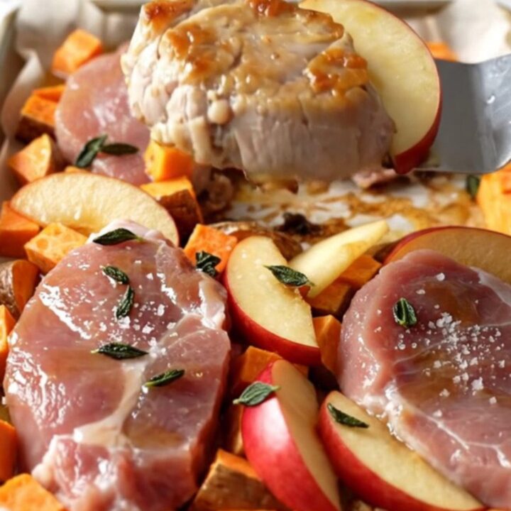 A sheet pan filled with golden-brown pork medallions, roasted sweet potato cubes, and tender red apple wedges.