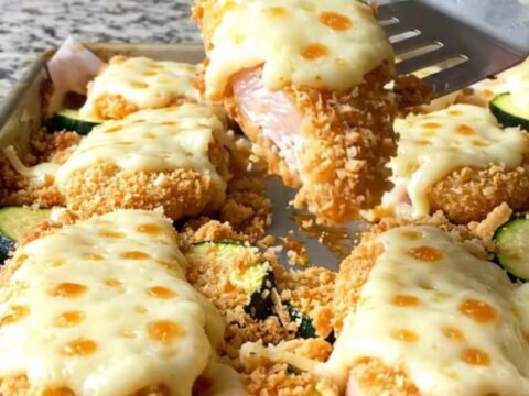 Crispy baked chicken parmesan tenders with melted cheese and tender zucchini on a sheet pan.