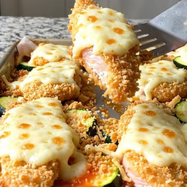Crispy baked chicken parmesan tenders with melted cheese and tender zucchini on a sheet pan.