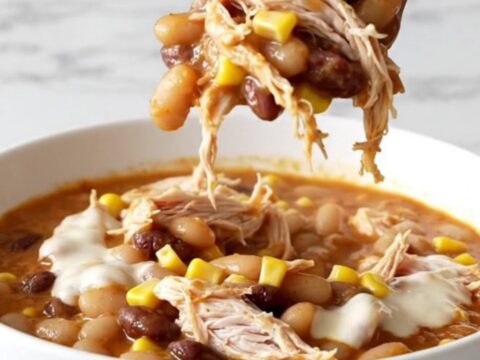 A top-down view of creamy slow cooker white queso chicken chili in a black stoneware insert on a white marble surface.