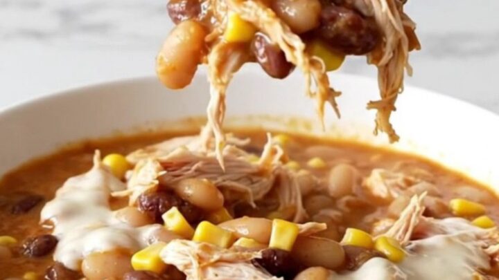 A top-down view of creamy slow cooker white queso chicken chili in a black stoneware insert on a white marble surface.