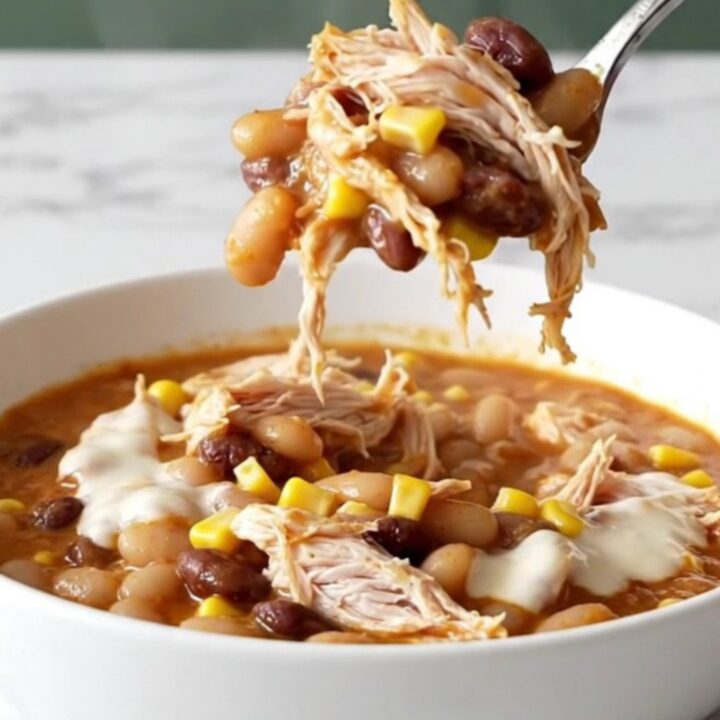 A top-down view of creamy slow cooker white queso chicken chili in a black stoneware insert on a white marble surface.