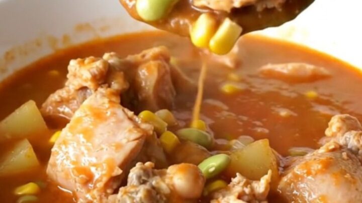 A bowl of hearty Kentucky chicken burgoo with visible chunks of chicken, potatoes, and corn in a rich tomato sauce.