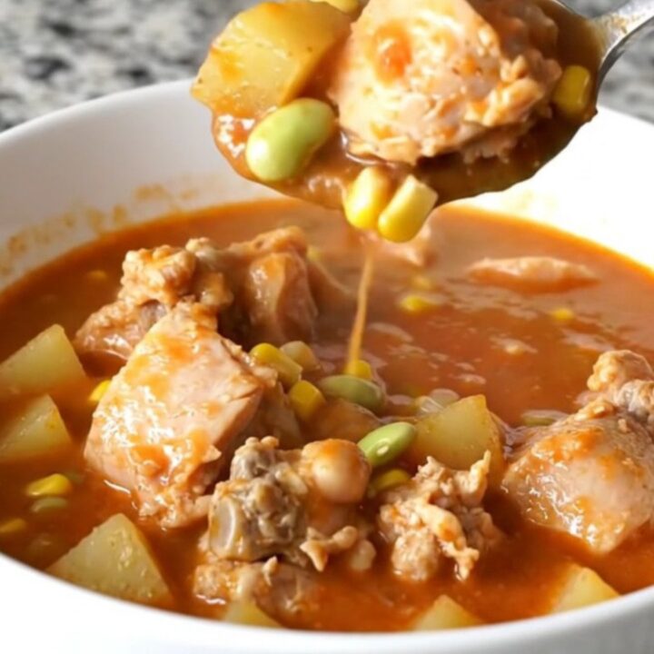 A bowl of hearty Kentucky chicken burgoo with visible chunks of chicken, potatoes, and corn in a rich tomato sauce.
