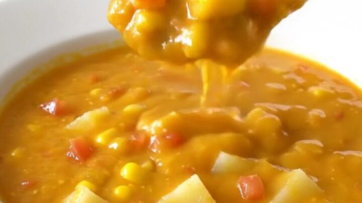 A bowl of creamy nacho potato soup with corn and tomatoes, steaming gently.