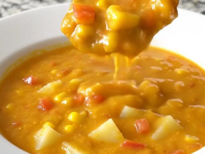 A bowl of creamy nacho potato soup with corn and tomatoes, steaming gently.