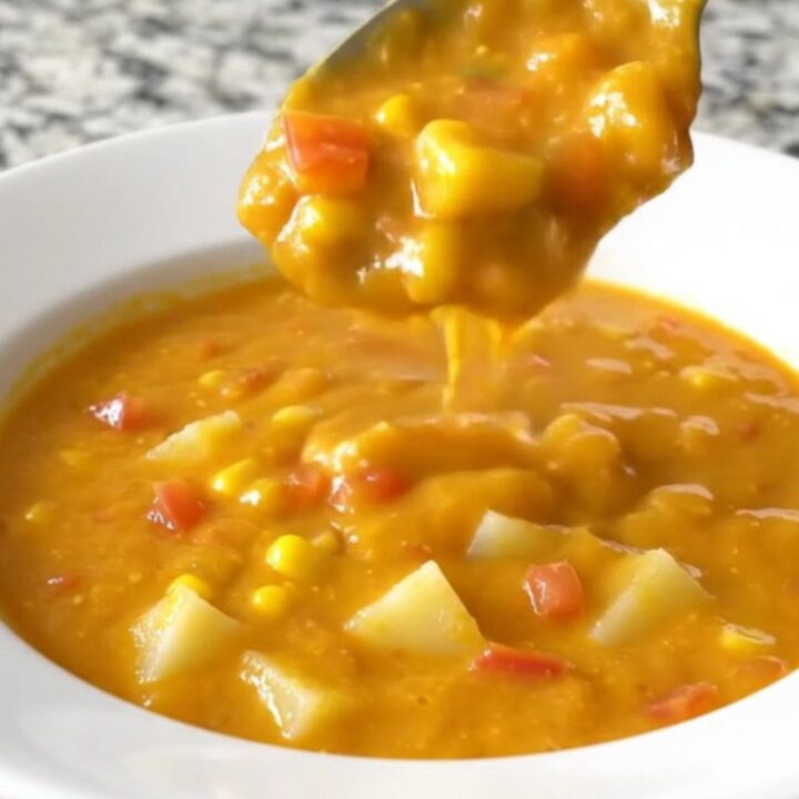 A bowl of creamy nacho potato soup with corn and tomatoes, steaming gently.