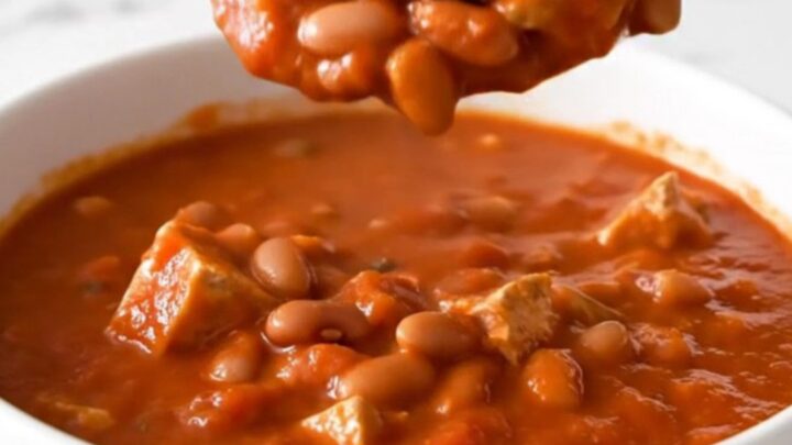 A top-down view of a black slow cooker filled with ground turkey, pinto beans, and a rich tomato-based chili.