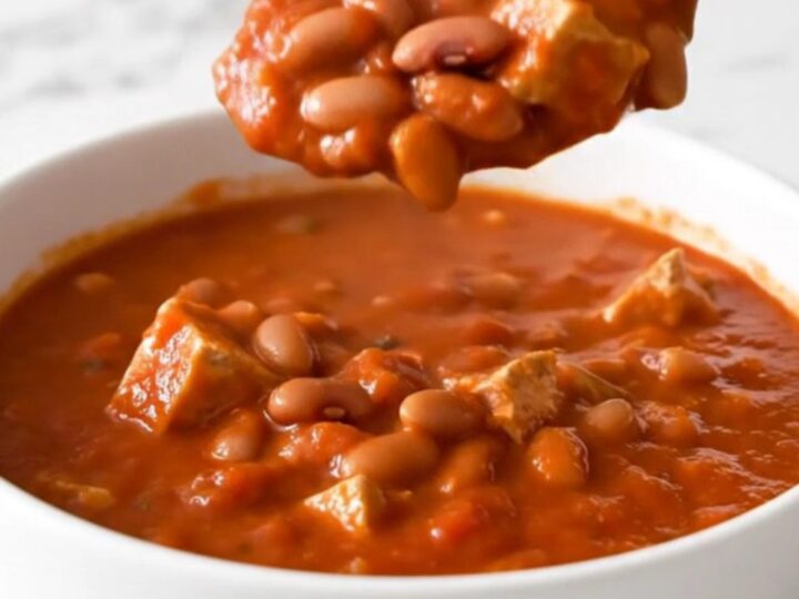 A top-down view of a black slow cooker filled with ground turkey, pinto beans, and a rich tomato-based chili.