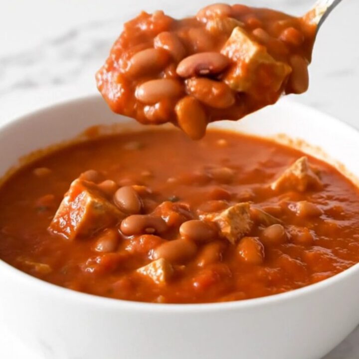 A top-down view of a black slow cooker filled with ground turkey, pinto beans, and a rich tomato-based chili.