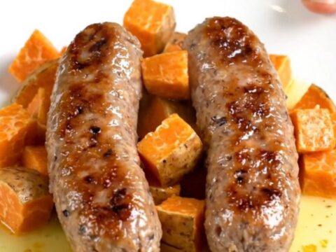 A close-up of slow-cooked Italian sausage links and tender sweet potato cubes in a savory sage-infused broth.