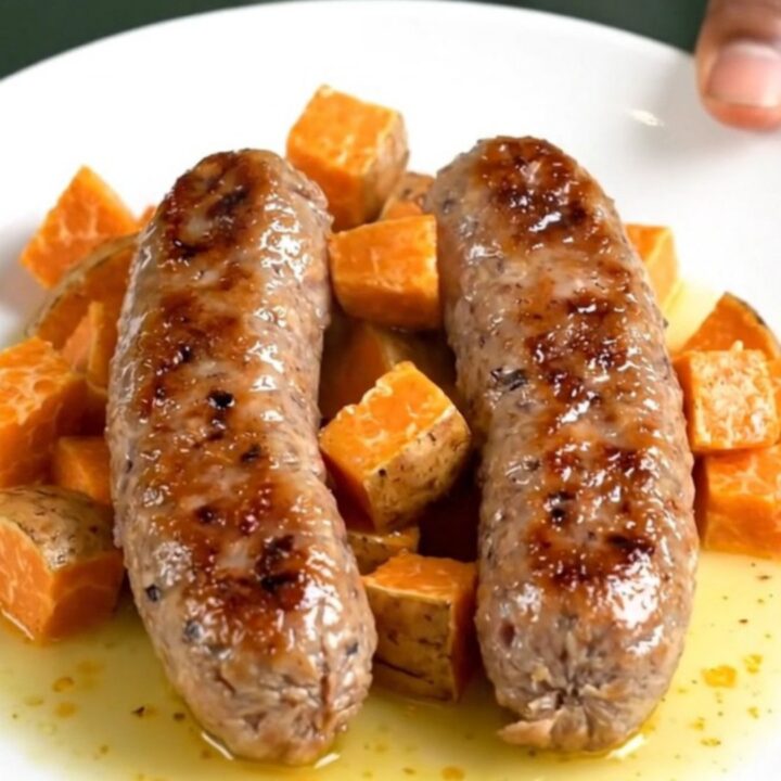 A close-up of slow-cooked Italian sausage links and tender sweet potato cubes in a savory sage-infused broth.