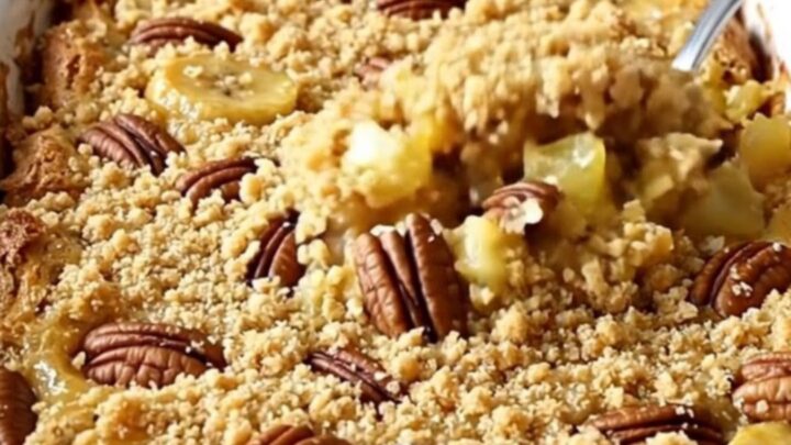 A golden-brown Hummingbird Dump Cake in a white ceramic dish with toasted pecans on top.