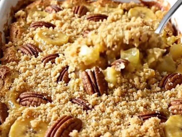 A golden-brown Hummingbird Dump Cake in a white ceramic dish with toasted pecans on top.
